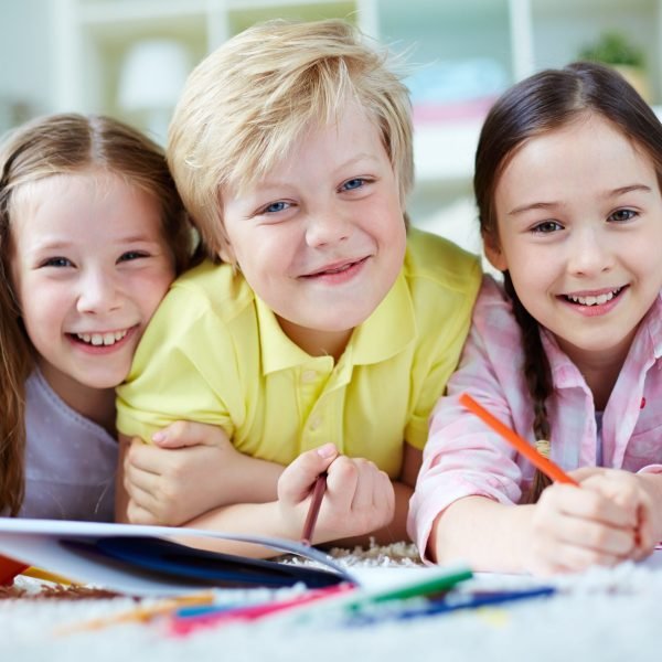 Two little girls and cute boy looking at camera while lying on the floor and drawing